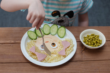 Ребенок ест макароны с колбасой и огурцами - obrazy, fototapety, plakaty
