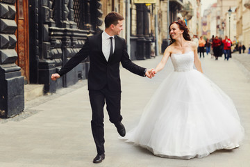 Naklejka premium Groom holds bride's hand tightly while they run along old buildi