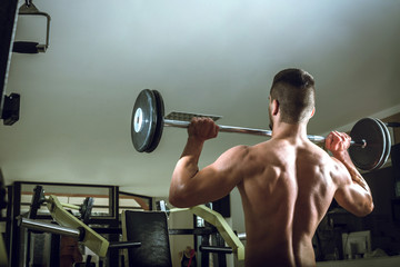 Young man lifting barbell. View from behind.