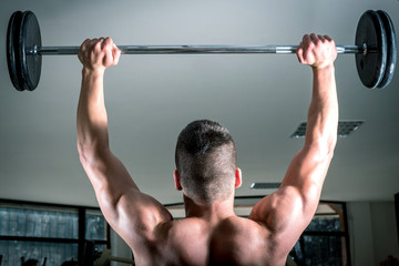 Naklejka premium Young man lifting barbell. View from behind.