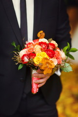 Groom holds a red bouquet of little roses