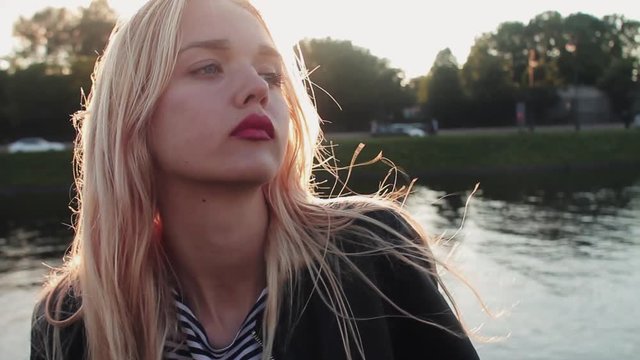 Young girl posing on the gren grass near the river at sunset