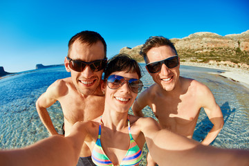 Fototapeta premium young happy couple friends on the beach taking selfie on sea background. Balos beach, Crete, Greece.