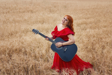 Naklejka na ściany i meble Woman in a red dress with a guitar in a barley field.