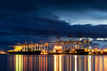 Fototapeta na wymiar Container Cargo freight ship with working crane bridge in shipyard at dusk for Logistic Import Export background