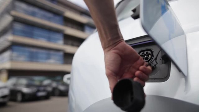 Color footage of a man's hand closing the lid of an electrical car, after charging.