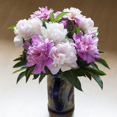 A bouquet of white and pink peonies in a stein on a brown background. 