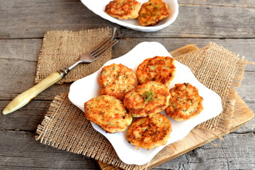 Fried red fish cutlets on a plate and on cutting board, fork on a burlap on an old wooden...