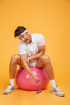 Sportsman man on fitness ball doing exercises with small dumbbells