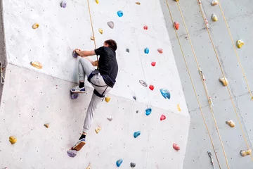 Rolgordijnen man climbing on artificial boulders wall indoor, rear view © EdNurg