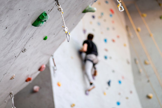 man climbing on practical wall indoor, securing carabiners and rope