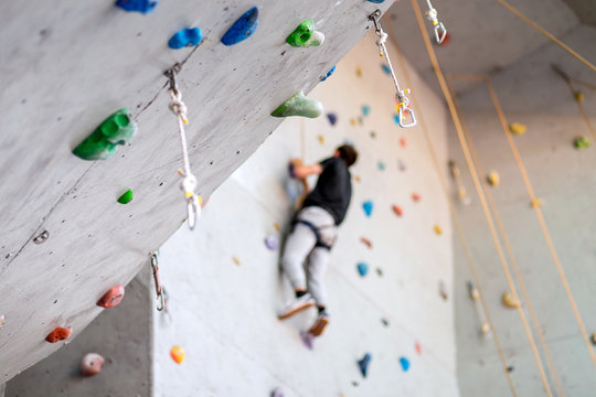 man climbing on practical wall indoor, securing carabiners and rope