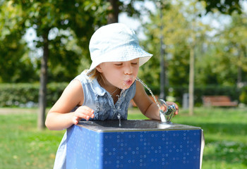 Cute baby girl drinking from water drinking fountain in summer