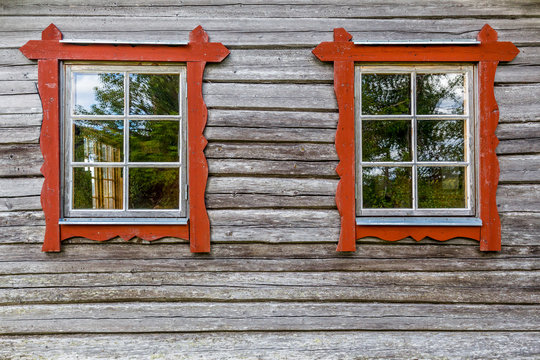 Two windows with red frames on log house wall, traditional style. 