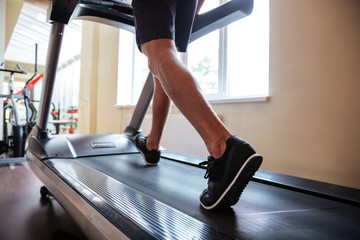 Legs of young fitness man running on treadmill in gym - Powered by Adobe