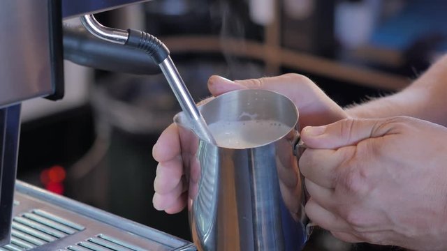 Barista steaming milk for cappuccino in coffee shop.