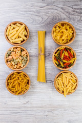 Various combinations of pasta on wooden background, burlap bags, bamboo bowls. diet and nutritional concept.