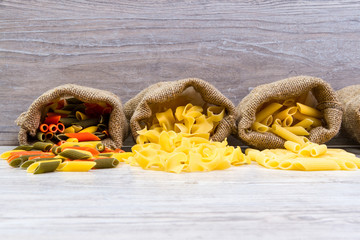 Various combinations of pasta on wooden background, burlap bags, bamboo bowls. diet and nutritional concept.