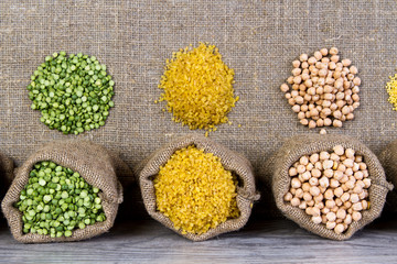 Set groats, peas, rice, millet, peas in sacks, burlap on wooden background