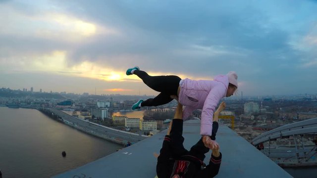 Young couple practicing acro yoga on top of bridge at sunset, extreme sports
