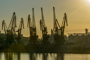 Obraz premium Port cranes against the evening sky in yellow tones on sunset
