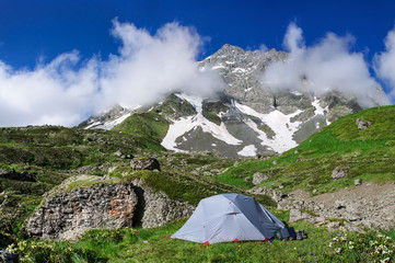 gray tent in grass on background of mountains and rocks