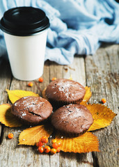 Chocolate cupcakes with a paper glass of coffee on a wooden surface, autumn composition