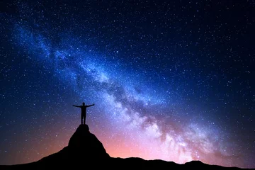 Afwasbaar fotobehang Night landscape with Milky Way. Silhouette of a standing man with raised up arms on the top of mountain. High rocks, mountain peak. Beautiful Galaxy.  Universe. Blue night starry sky and city lights © den-belitsky