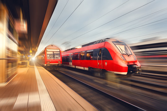 Fototapeta Modern high speed red passenger trains at sunset. Railway station in Nuremberg, Germany. Railroad with motion blur effect. Industrial concept landscape