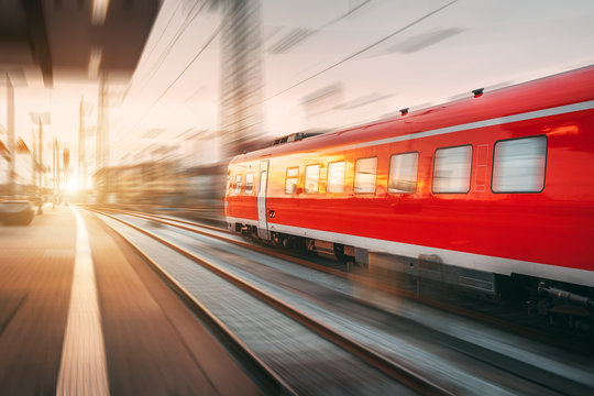 Fototapeta Modern high speed red passenger train moving through railway station in the evening. Railway station at sunset in Nuremberg, Germany. Railroad with motion blur effect. Industrial concept landscape