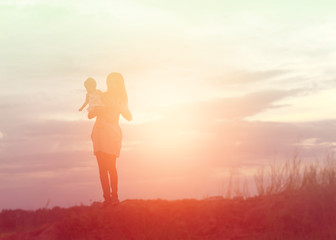 Mother holding baby walking on the sunset background.
