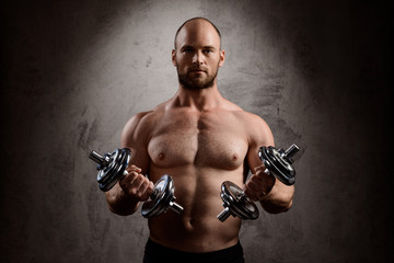 Obraz na płótnie Canvas Young powerful sportsman training with dumbbells over dark background.