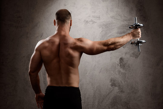 Young powerful sportsman training with dumbbells over dark background.