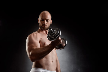 Fototapeta na wymiar Young powerful sportsman training with dumbbells over black background.