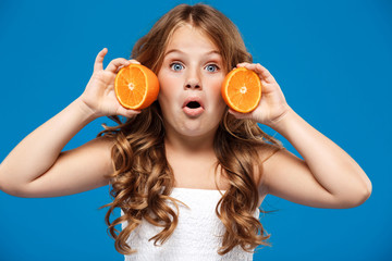 Surprised young pretty girl holding oranges over blue background.