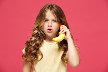 Young pretty girl holding banana like phone over pink background.