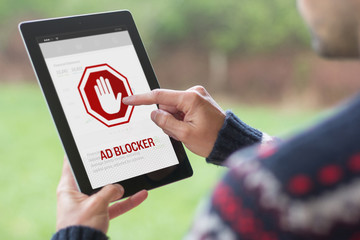 Young man using his tablet with ad blocker on the screen - obrazy, fototapety, plakaty