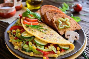 Omelet with pepper, tomato, corn, green onion, cucumber, mushrooms and fried bread on a wooden background