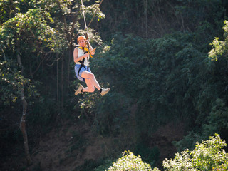 Brave woman in helmet and harness zip lining at adventure park on the background of a deep abyss