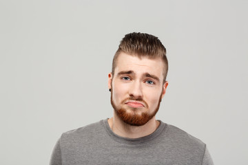 Upset young handsome man posing over grey background. Copy space.