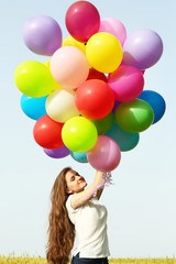 Fototapeta na wymiar Happy woman with colorful balloons in field on blue sky background