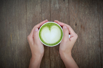 Hand holding cup of Matcha latte art Green tea coffee on wood table