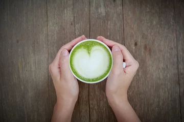 Papier Peint photo autocollant Theé Hand holding cup of Matcha latte art Green tea coffee on wood table