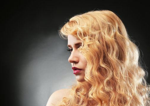 Portrait of young woman with blonde hair on dark background
