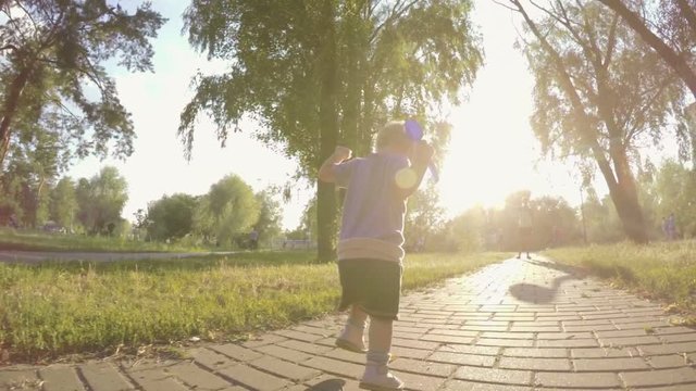 Little girl makes the first steps in a summer park, falls and self-raised and continues to go, low wide angle shooting, slow motion