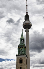 View of church tower in front of television tower with cloudy background