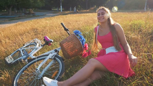 Young attractive girl sitting on grass with vintage bike in park at sunset