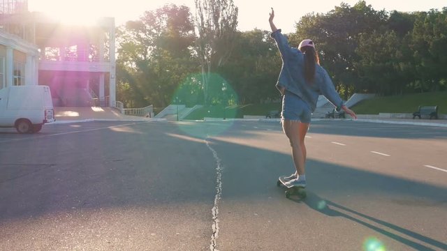 Young attractive girl riding on longboard in park during sunrise, slow motion