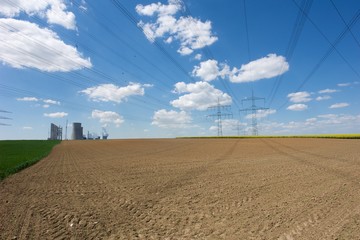 Kraftwerk mit Strommasten und einem blauen Himmel an einem abgeernteten Feld