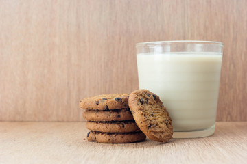 Chocolate chip cookies and a glass of milk on a wooden background.